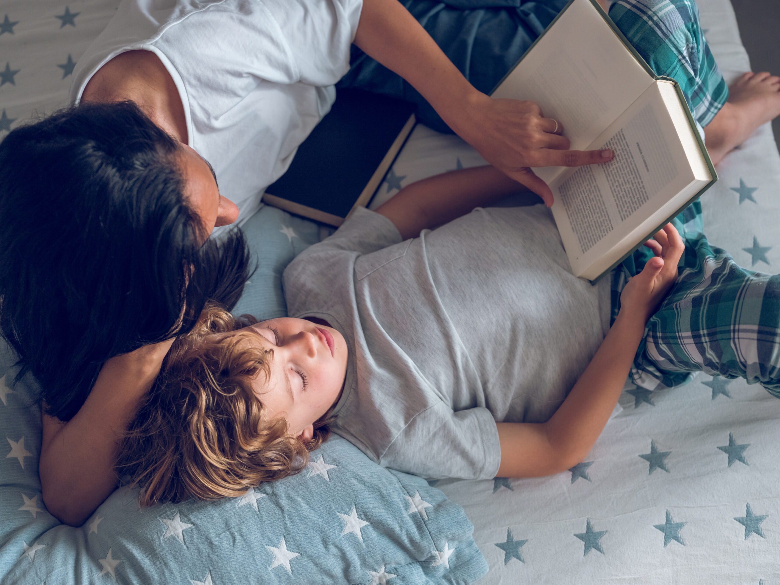 A mother and son reading a book from a series together at bedtime.