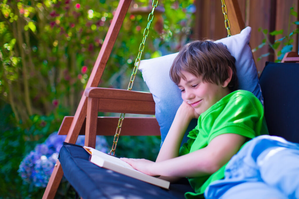 A boy happily reading on a porch swing