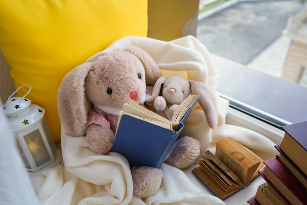 A cozy reading corner with books, a blanket and stuffed animals.
