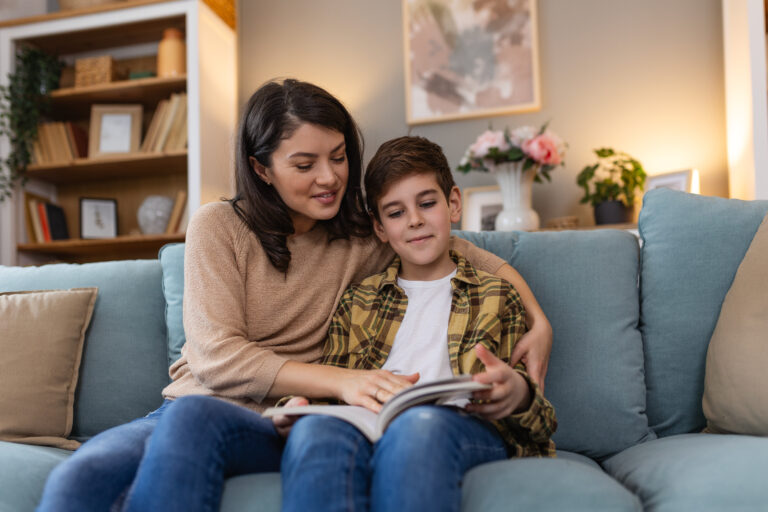 Mother and son snuggle on the couch enjoying a story together.