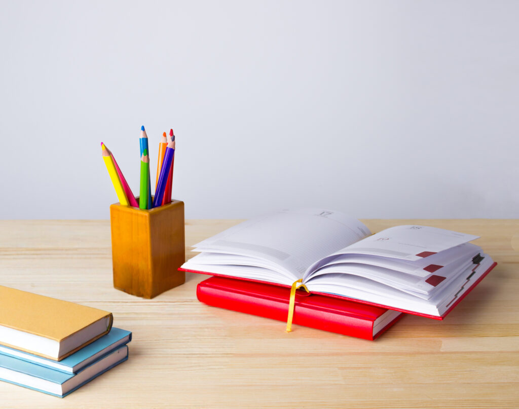 An open planner with colored pencils and a stack of books nearby